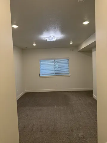 Carpeted room featuring a window with horizontal blinds, recessed ceiling lighting, and a decorative flush-mount ceiling fixture