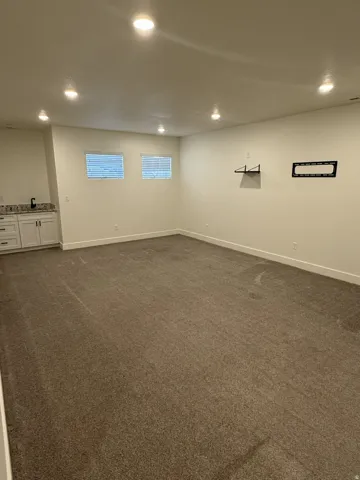 Spacious room featuring neutral carpeting, recessed ceiling lighting, and a built-in wet bar with white cabinetry, a dark countertop, and a black faucet