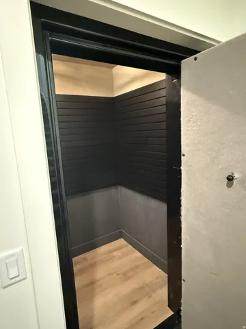 Secure walk-in space featuring a heavy-duty door, wood-finish flooring, dark horizontal slat paneling, and a light-toned ceiling