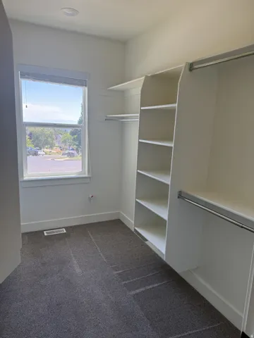 Walk-in closet featuring built-in shelving, chrome hanging rods, a window, recessed lighting, and grey carpet flooring