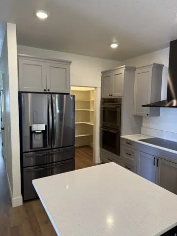 Contemporary kitchen featuring a white quartz-finish island countertop, stainless steel refrigerator, built-in double oven, sleek cooktop, and a walk-in pantry with ample shelving