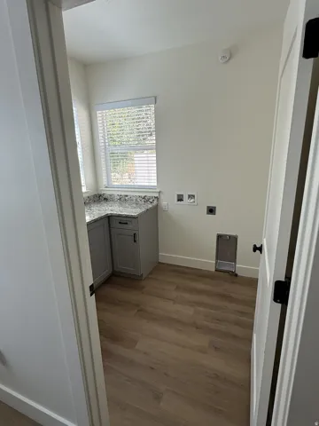 Functional utility space featuring a corner countertop with gray cabinetry, a window with blinds, and wood-finish flooring