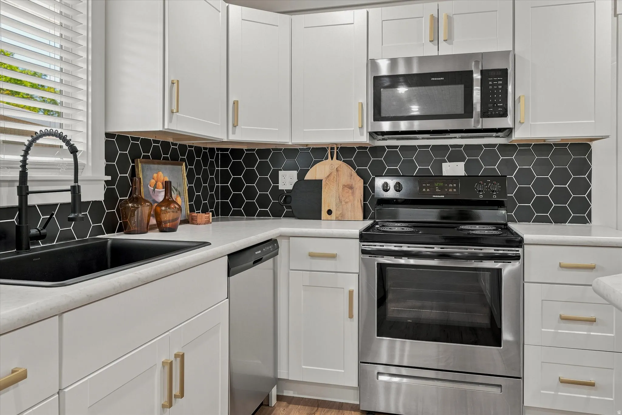 Modern kitchen featuring white shaker-style cabinetry with gold-tone hardware, a black hexagon tile backsplash, and light-toned countertops