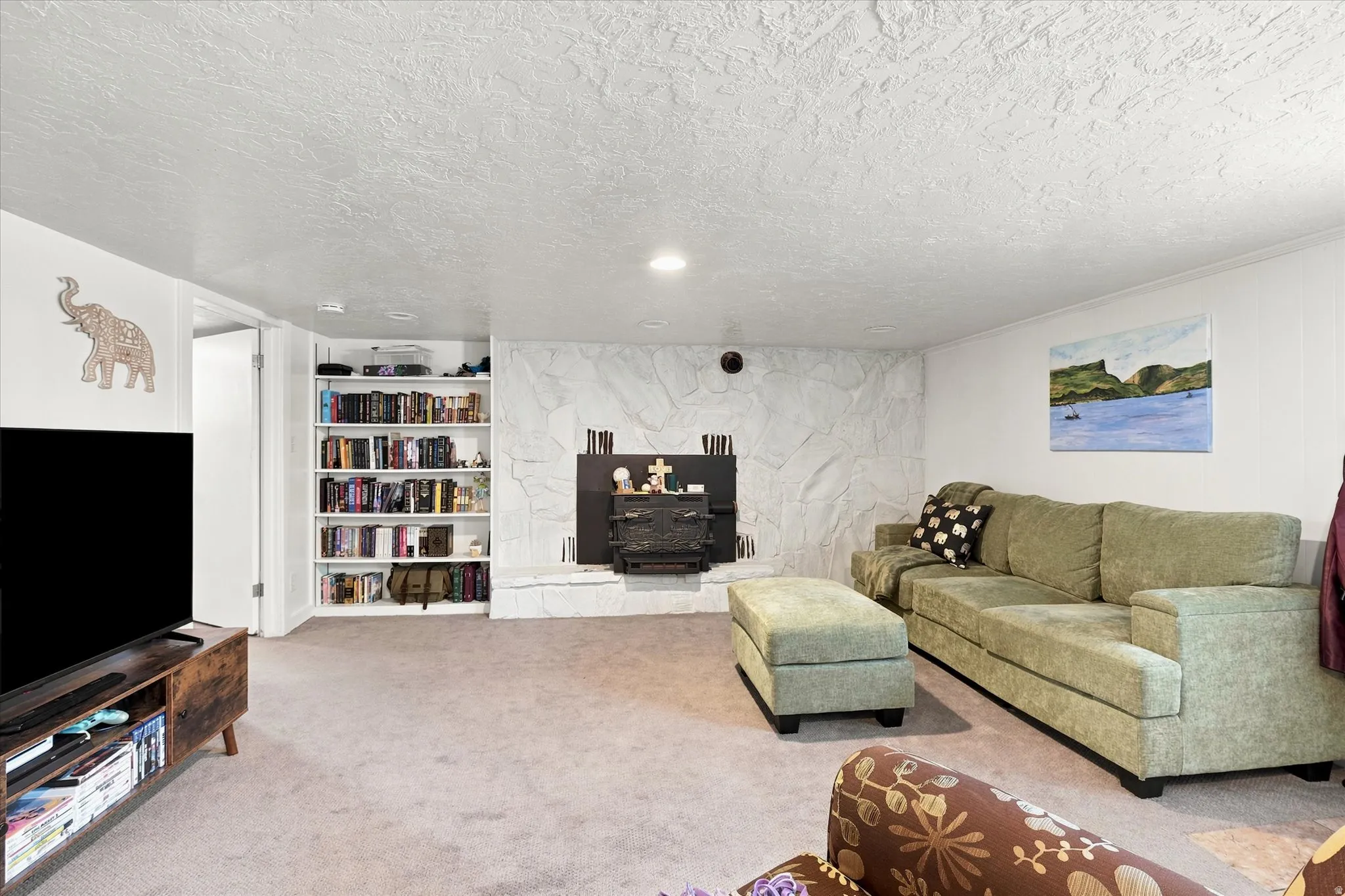 Carpeted room featuring a stone fireplace with a wood stove insert, built-in shelving, and recessed lighting