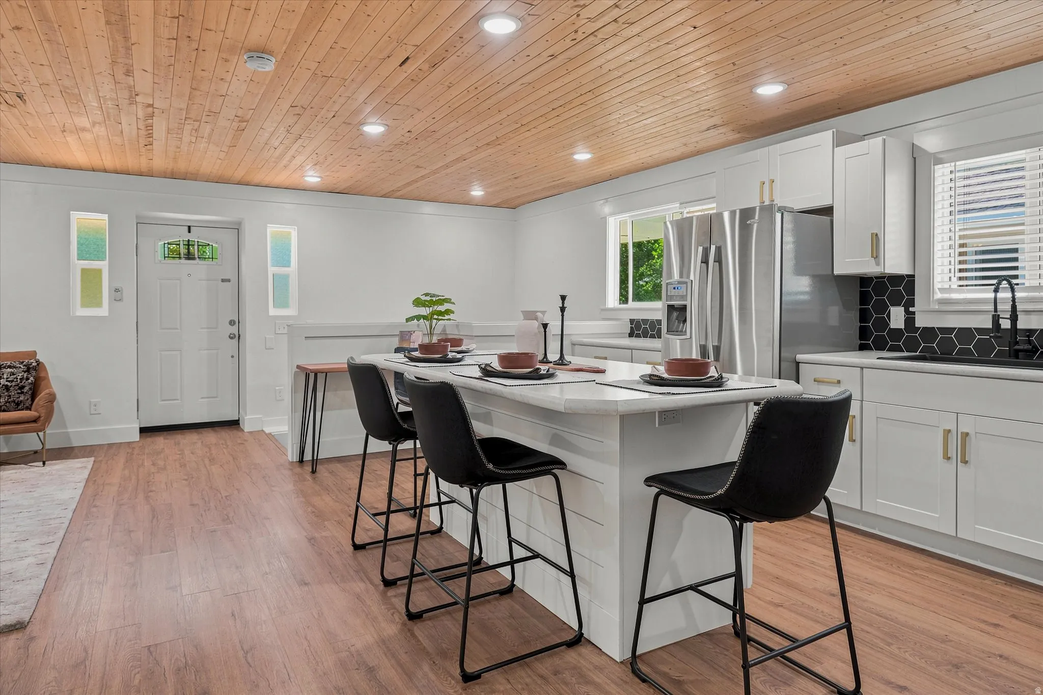 Open-concept kitchen and living area featuring wood-finish flooring, a wood-plank ceiling with recessed lighting, and a kitchen island with seating