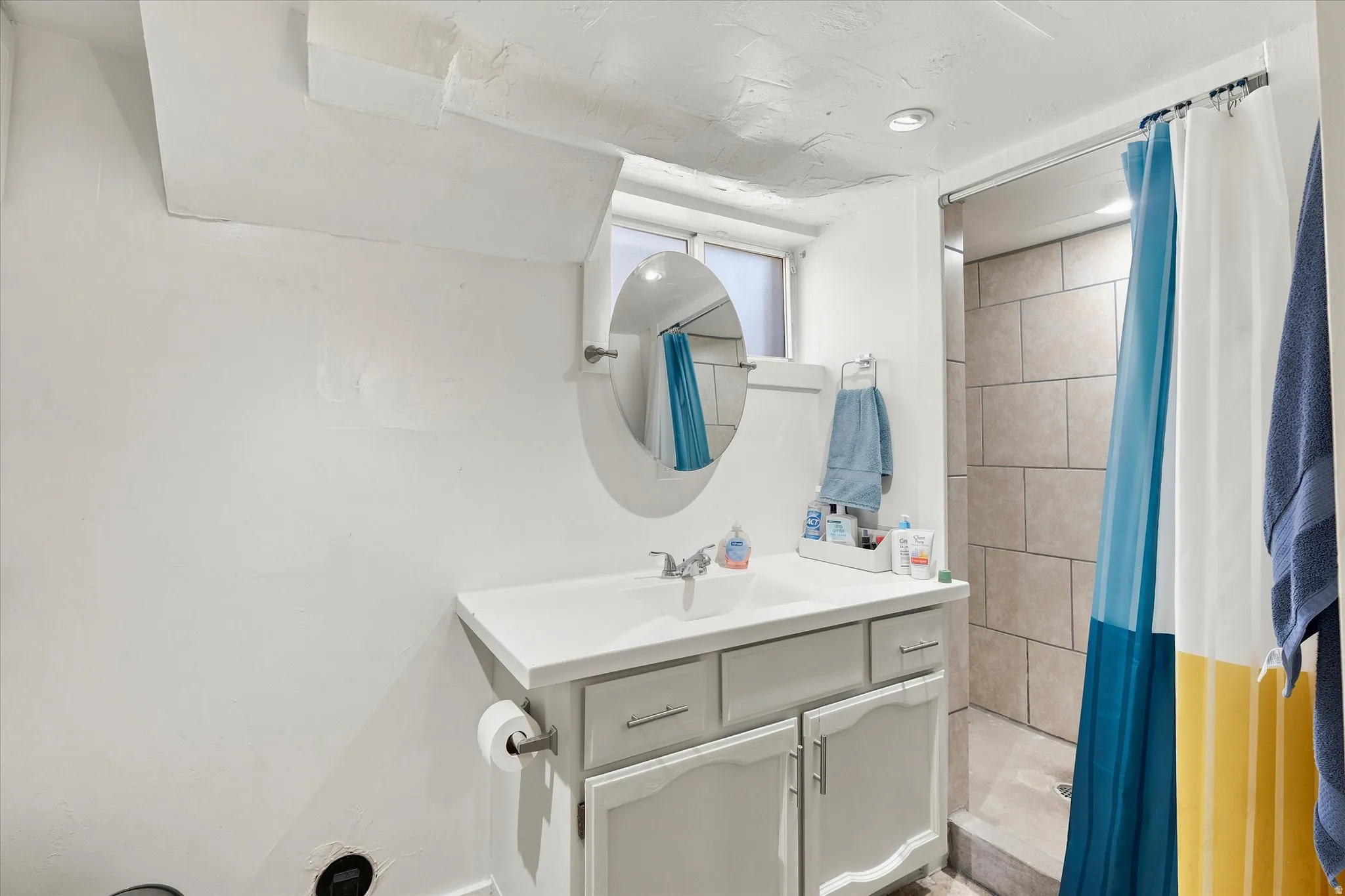 Vanity with white countertop and gray cabinetry, integrated sink, and an oval mirror
