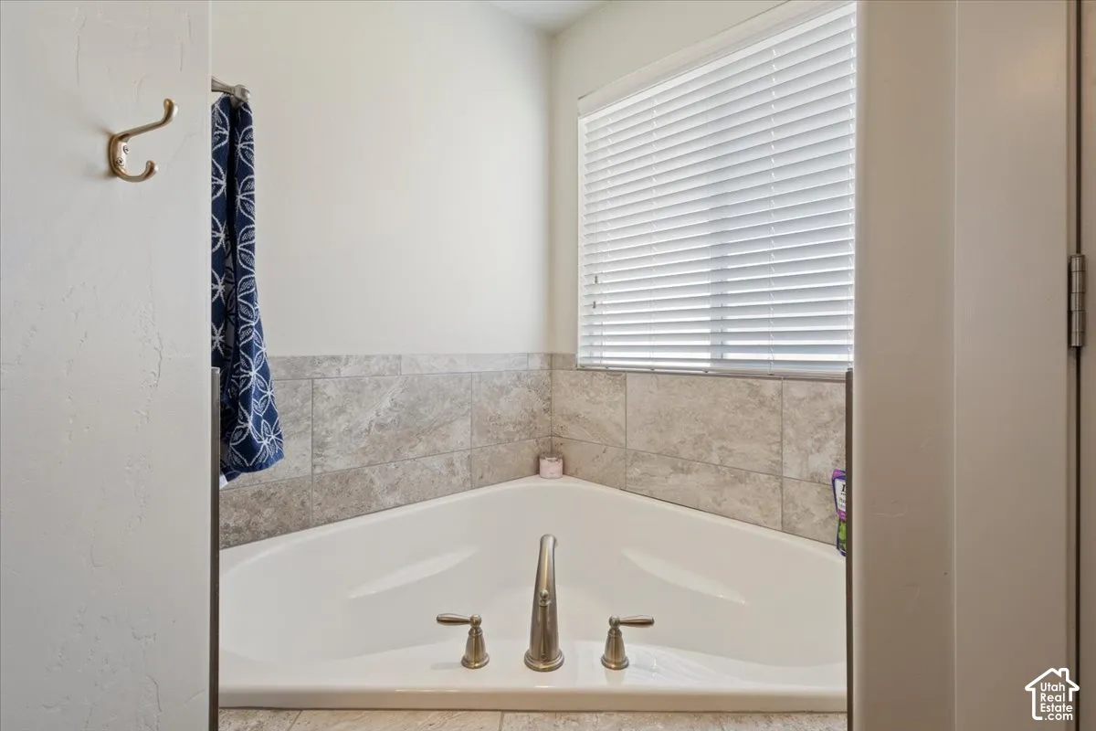 Corner soaking tub featuring a brushed nickel faucet and tile surround