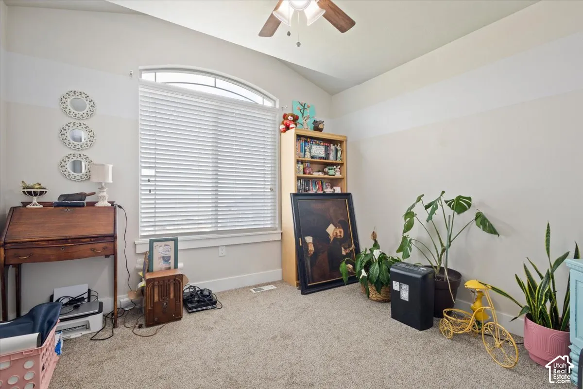Carpeted room featuring a large arched window with blinds, a vaulted ceiling, and a ceiling fan with light fixture
