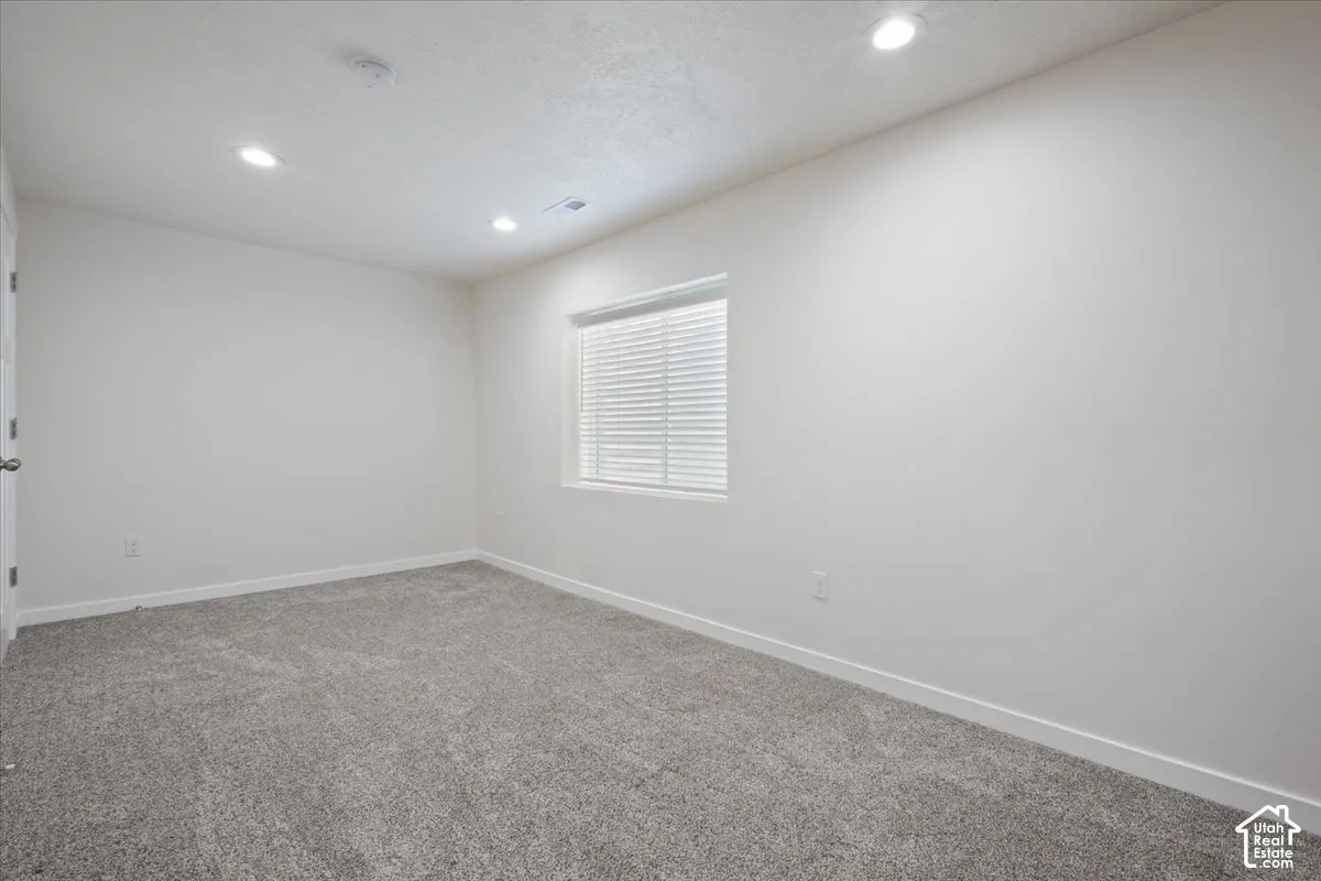 Neutral-toned room featuring a window with horizontal blinds, recessed lighting, and grey carpet flooring