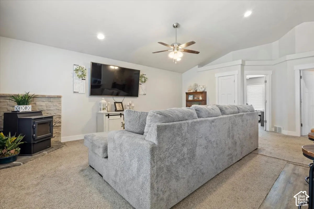 Living area featuring a stone accent wall, wood-burning stove, vaulted ceilings, and a ceiling fan