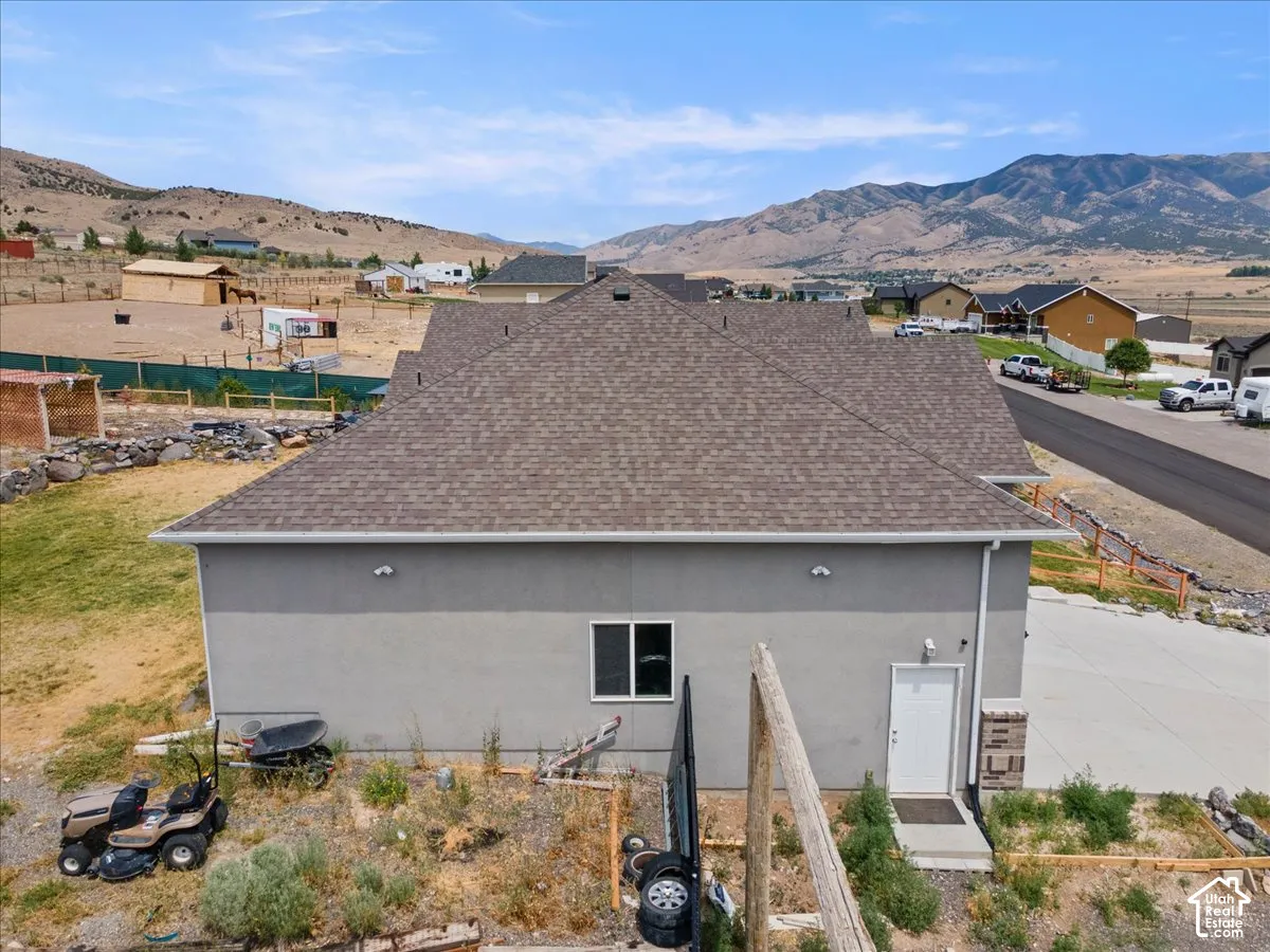 Contemporary residential structure featuring a gray stucco exterior, a brown shingle roof, and a white entry door with stacked stone details
