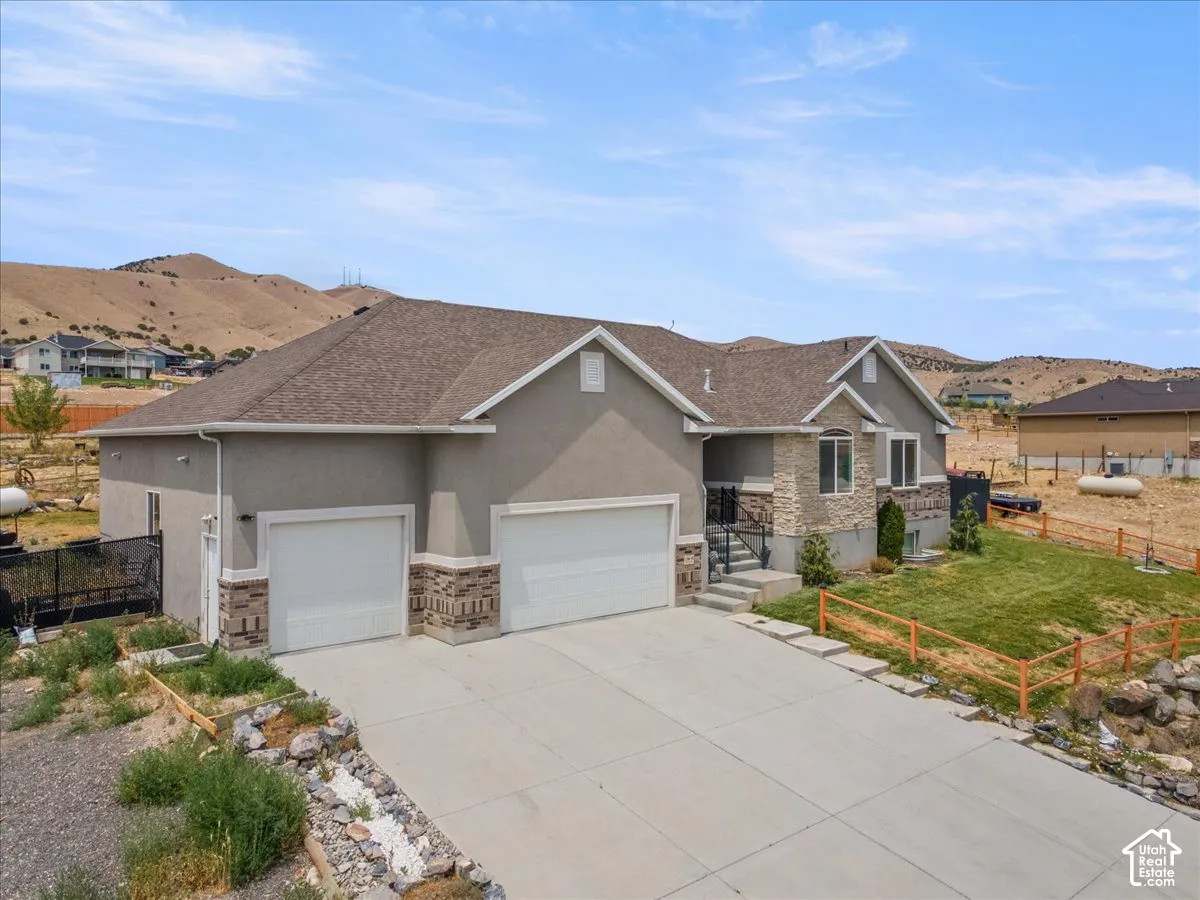 Contemporary residence featuring a stucco and stone facade with a multi-car garage, a concrete driveway, and a partially landscaped front yard