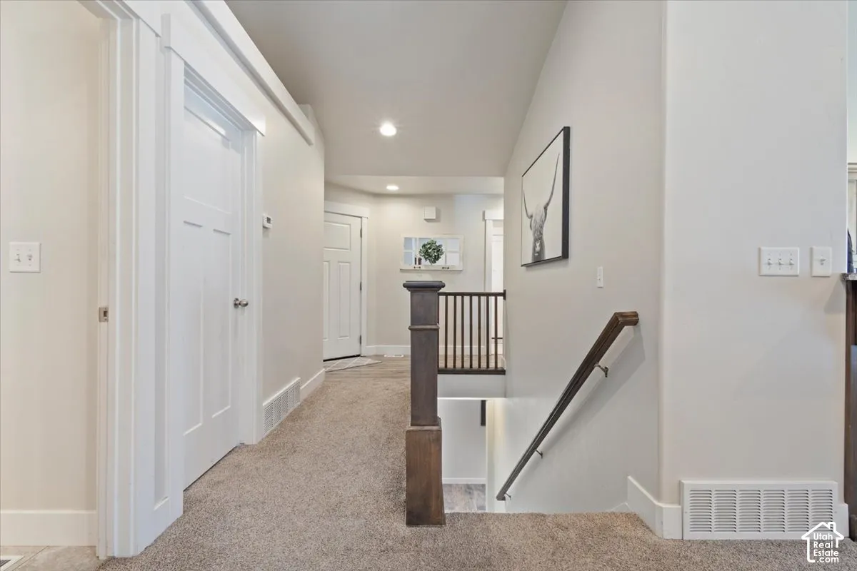 Carpeted hallway featuring a staircase with wood newel posts, dark wood handrail, and white balusters