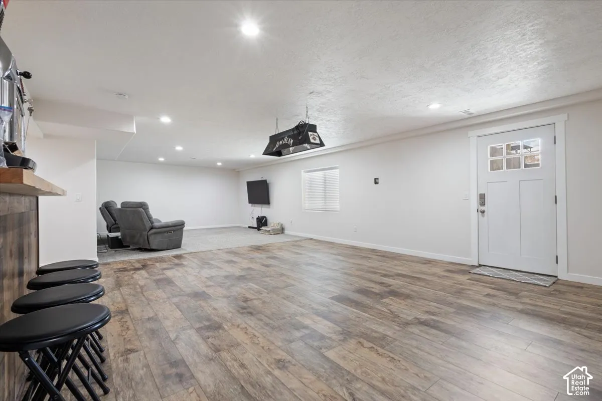 Spacious room featuring wood-finish flooring, recessed lighting, and a built-in bar with a solid wood countertop and wood paneling