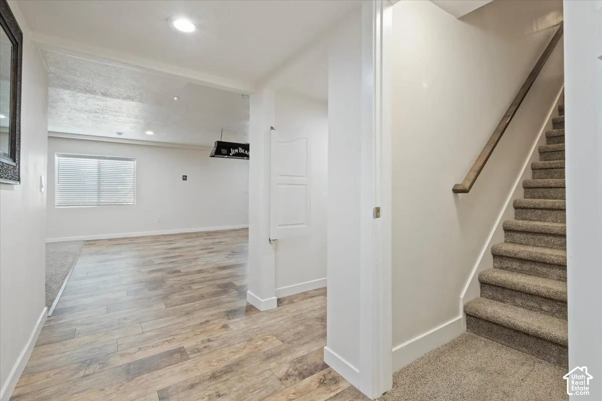 Entryway featuring wood-finish flooring, a carpeted staircase with a wood handrail, recessed lighting, and a white paneled door