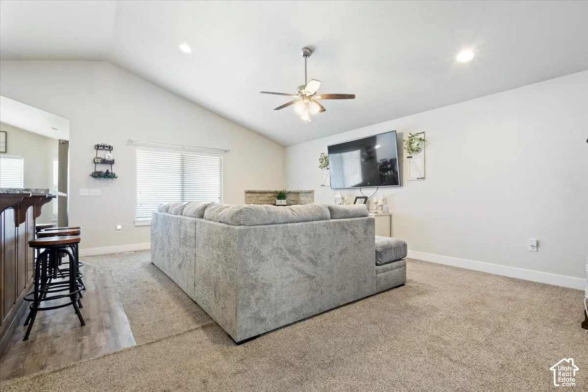 Open-concept living space featuring vaulted ceilings, a ceiling fan with integrated lighting, recessed lighting, and an entertainment wall
