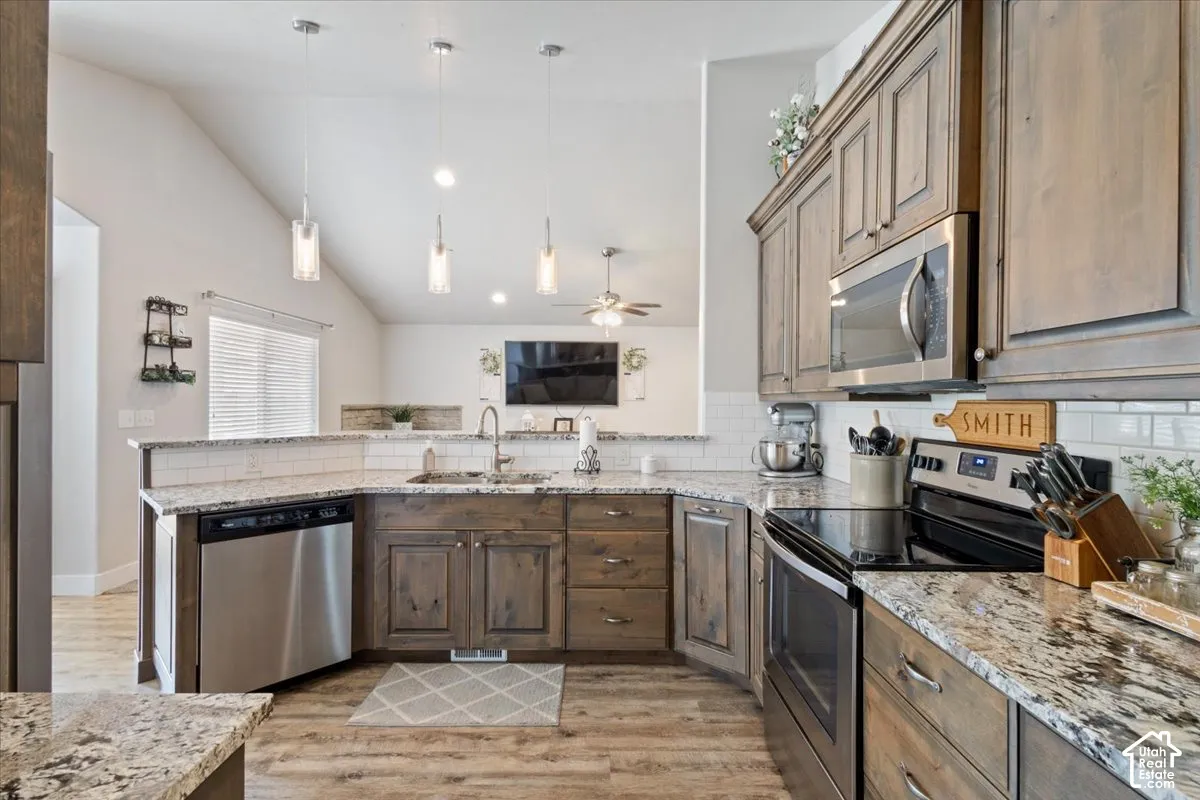 Kitchen featuring wood-finish cabinetry, granite-style countertops, stainless steel appliances, a subway tile backsplash, and wood-finish flooring