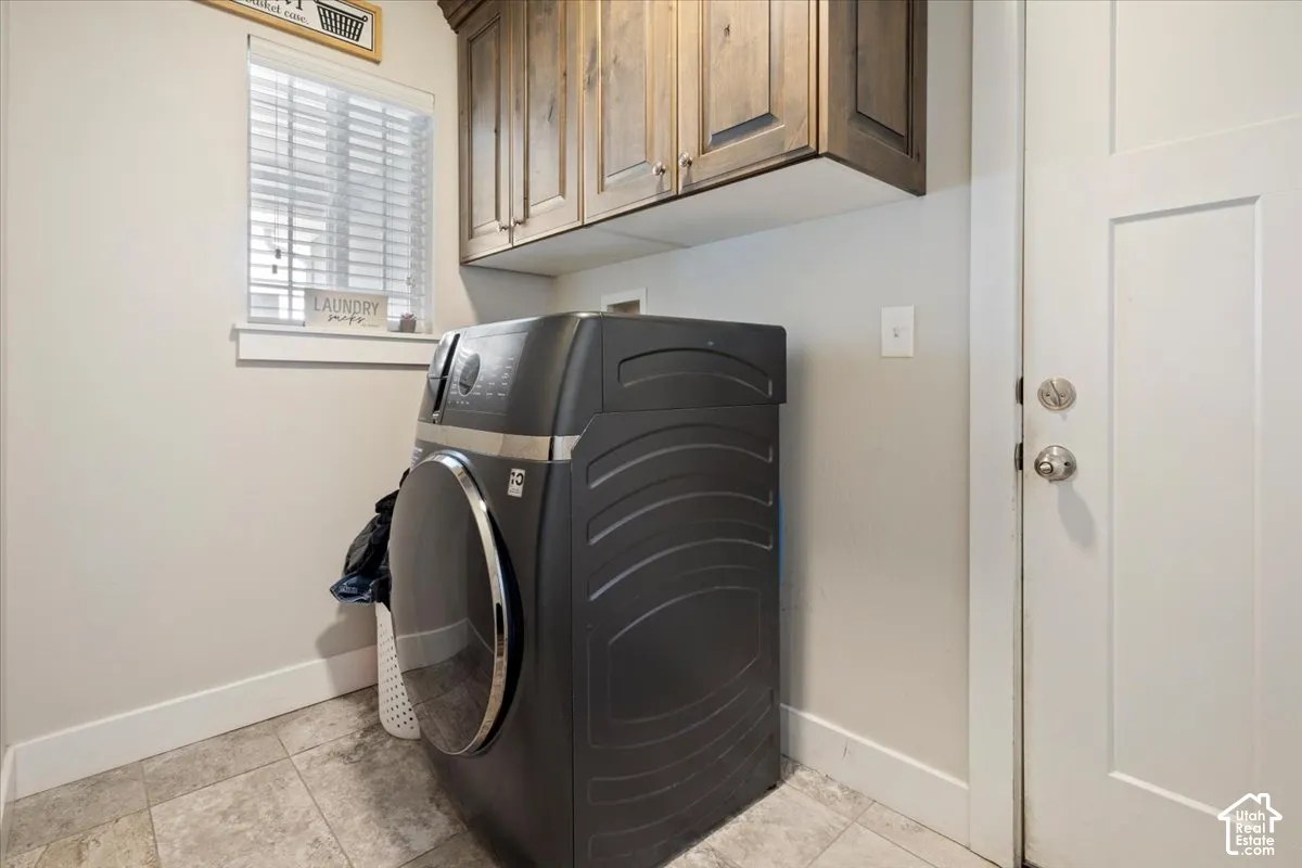 Dedicated laundry area featuring overhead wood cabinetry and tile flooring