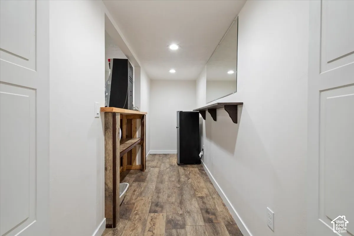 Hallway featuring wood-finish flooring, white paneled doors, recessed lighting, a wall-mounted mirror, and a floating shelf
