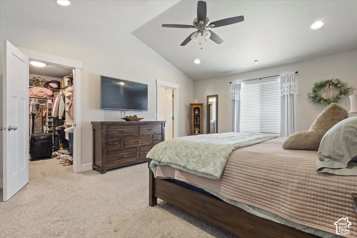Carpeted bedroom featuring a vaulted ceiling with a ceiling fan, recessed lighting, and a walk-in closet with an interior light
