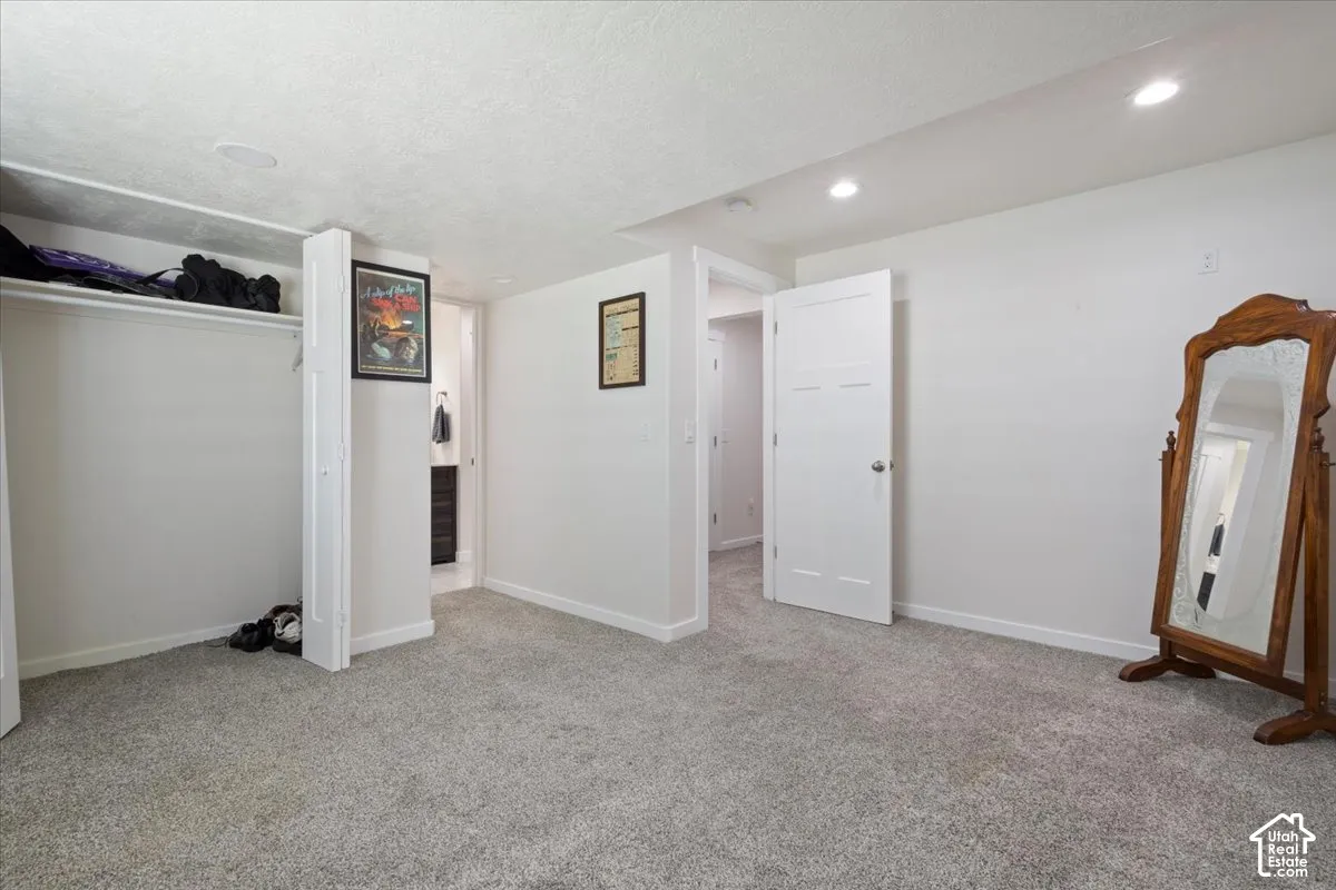 Spacious room featuring light gray carpeting, crisp white walls, recessed lighting, and a built-in closet with shelving