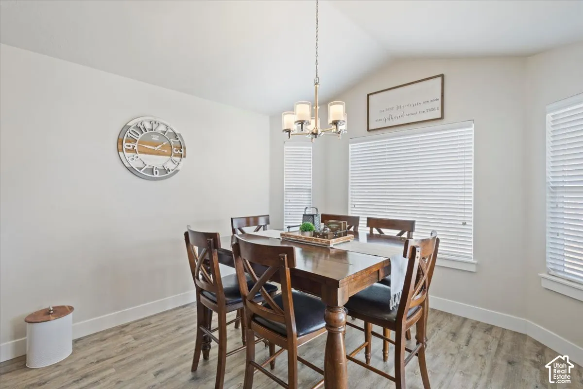 Dining area featuring a vaulted ceiling, wood-finish flooring, and multiple windows with blinds