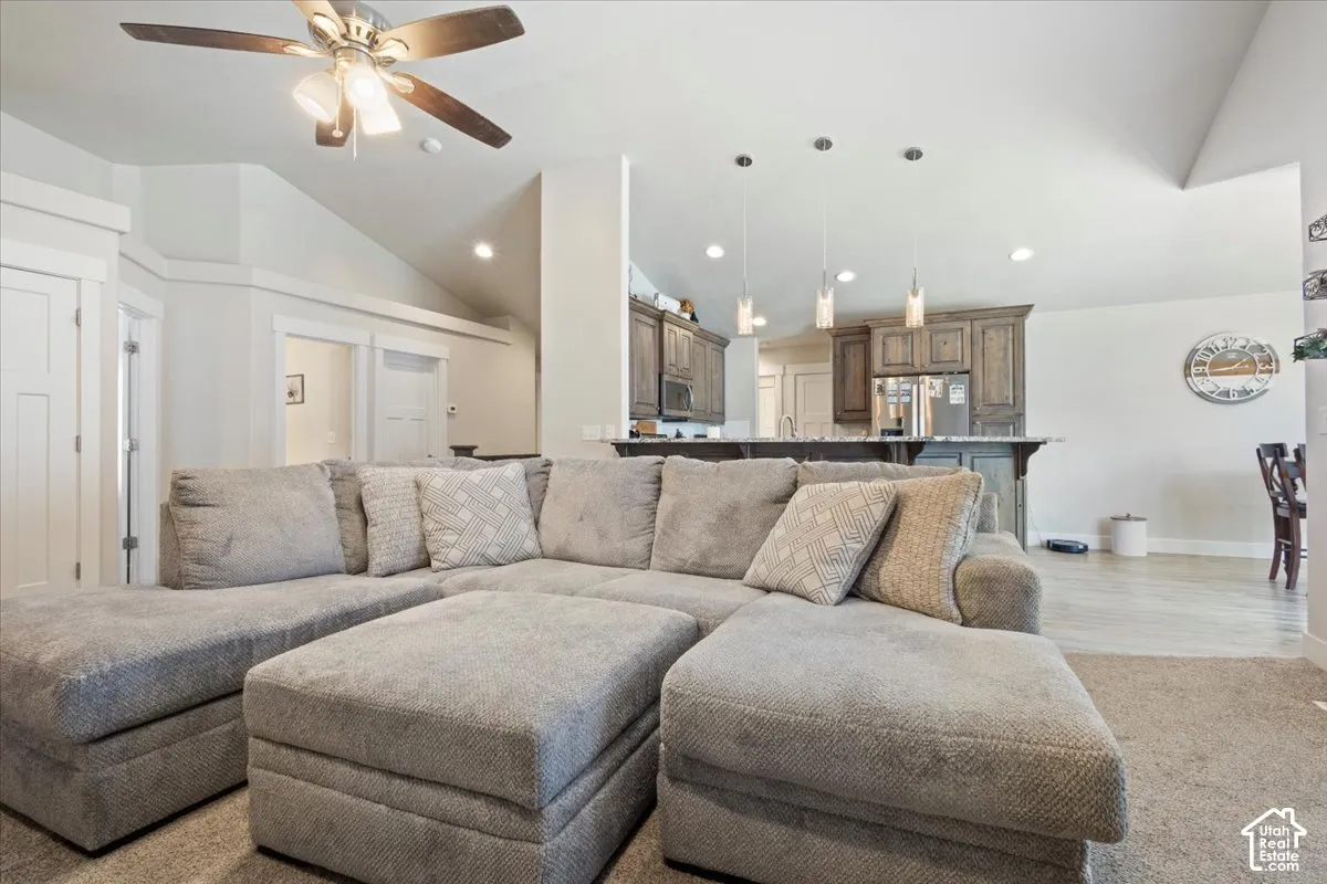 Spacious living area featuring a vaulted ceiling with a ceiling fan, recessed lighting, and durable carpeting