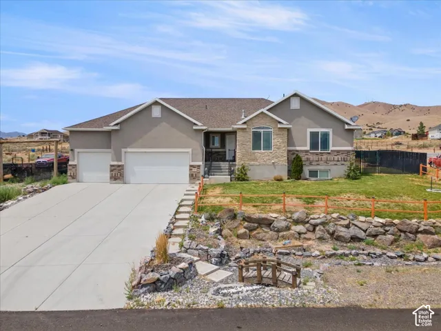 Contemporary residence featuring a stucco and stone facade, concrete driveway, two-car garage, and a tiered rock landscaping