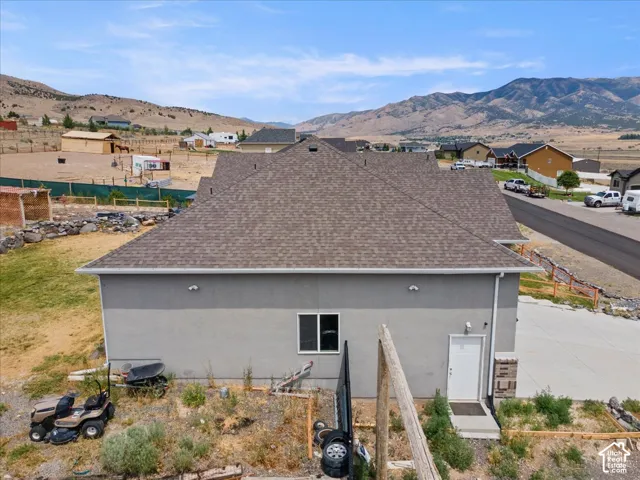 Contemporary residential structure featuring a gray stucco exterior, a brown shingle roof, and a white entry door with stacked stone details