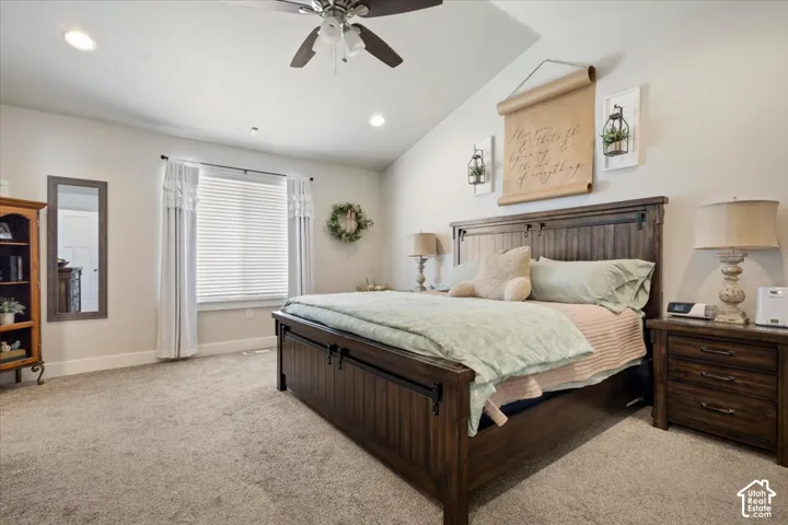 Vaulted ceiling bedroom featuring plush carpeting, a large window with blinds and drapes, and recessed lighting