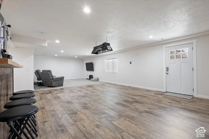 Spacious room featuring wood-finish flooring, recessed lighting, and a built-in bar with a solid wood countertop and wood paneling
