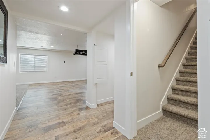 Entryway featuring wood-finish flooring, a carpeted staircase with a wood handrail, recessed lighting, and a white paneled door