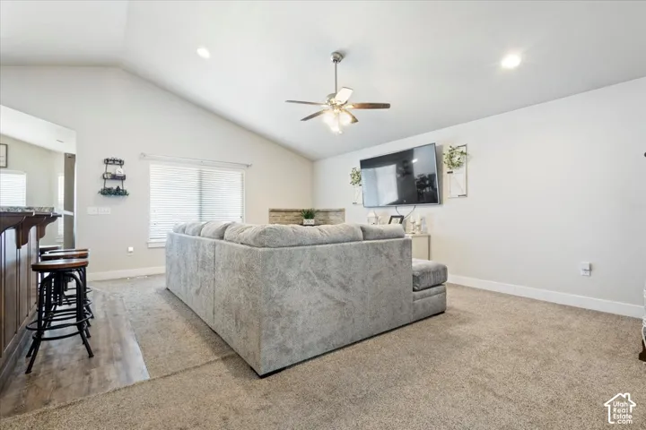 Open-concept living space featuring vaulted ceilings, a ceiling fan with integrated lighting, recessed lighting, and an entertainment wall