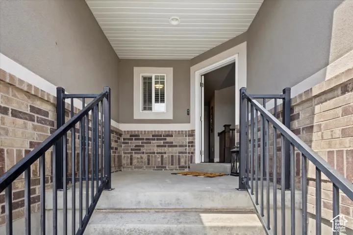 Inviting front porch featuring a brick facade, stucco siding, concrete stairs, and dark metal railings