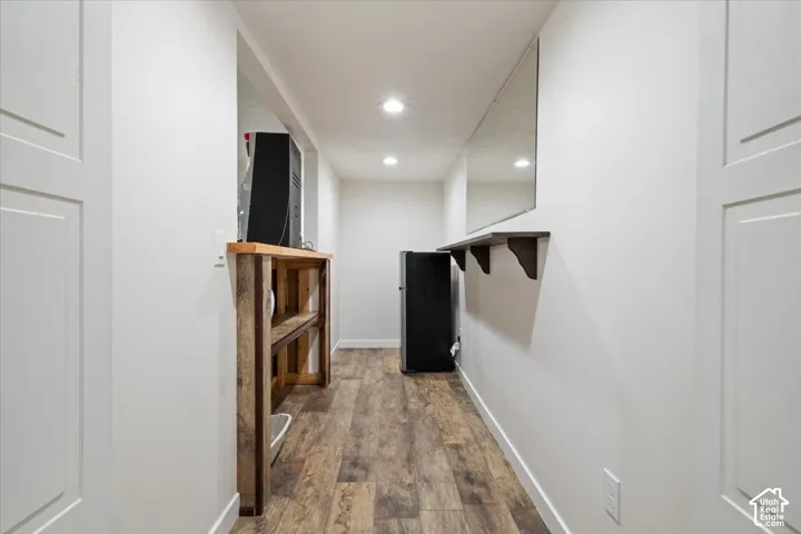 Hallway featuring wood-finish flooring, white paneled doors, recessed lighting, a wall-mounted mirror, and a floating shelf