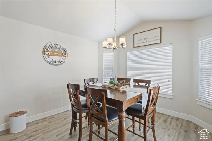 Dining area featuring a vaulted ceiling, wood-finish flooring, and multiple windows with blinds