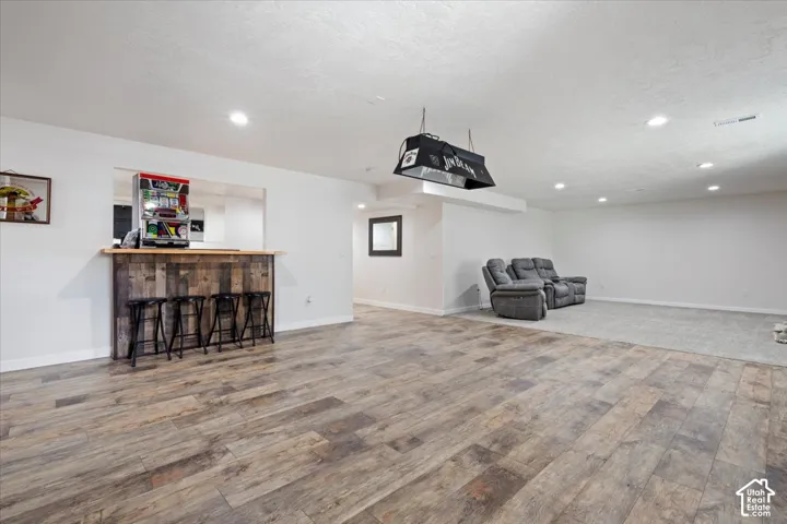 Spacious room featuring wood-finish flooring, a built-in bar with a wooden facade, recessed lighting, and a suspended light fixture