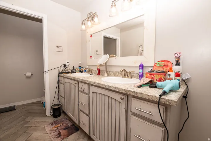 Bathroom vanity featuring dual sinks with individual faucets, a large framed mirror, and overhead vanity lighting