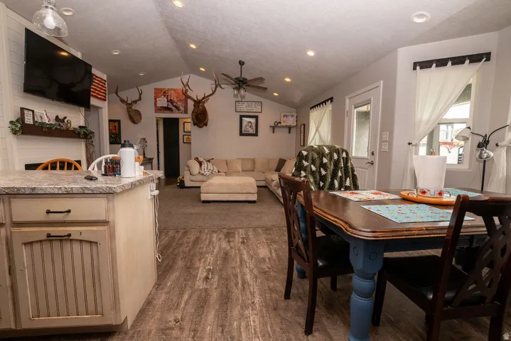 Open-concept living space featuring wood-finish flooring, vaulted ceilings with recessed lighting, and a kitchen island with a stone-look countertop