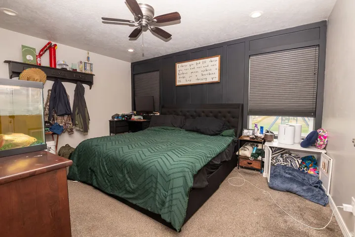 Bedroom featuring a dark accent wall with vertical paneling, a ceiling fan with integrated lighting, recessed lighting, and a window with blinds