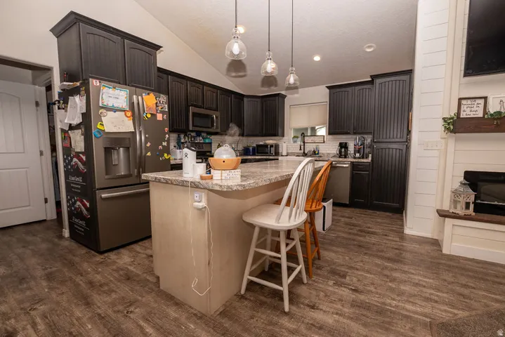 Kitchen featuring dark cabinetry, stainless steel appliances, a center island with a light-toned base and a light-toned countertop, wood-finish flooring, and pendant lighting