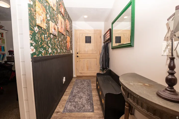 Entryway featuring wood-finish flooring, a wood-paneled door with a square window, and a wall with dark wainscoting topped by floral wallpaper
