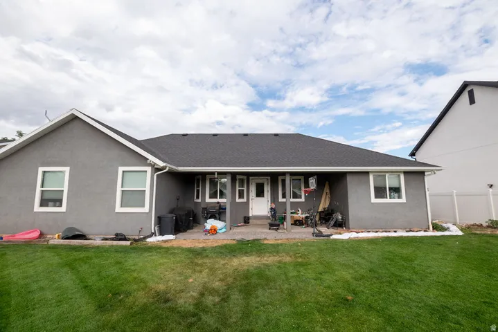 Rear exterior featuring a gray stucco finish, dark shingle roof, white trim, and a concrete patio