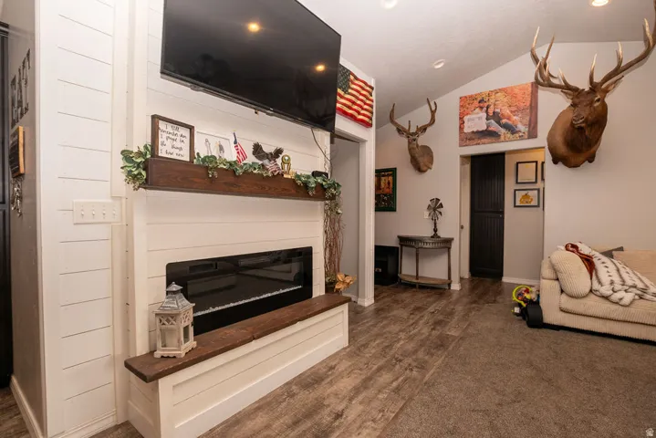Vaulted ceiling living area featuring an electric fireplace with a wood mantel, shiplap accent wall, wood-finish flooring, and recessed lighting