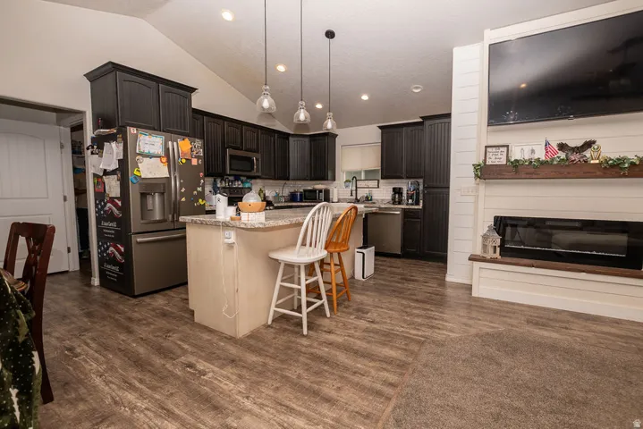 Open-concept living space featuring vaulted ceilings, wood-finish flooring, and a fireplace with a shiplap surround
