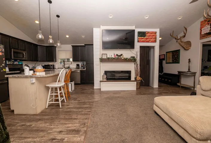 Open-concept living area featuring a modern fireplace with shiplap accent wall, wood-finish flooring, and a kitchen with dark cabinetry and a light-toned island with seating