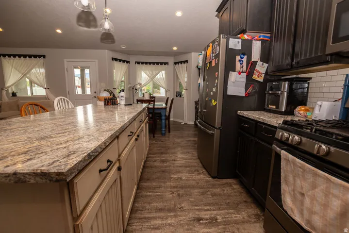 Spacious kitchen featuring an extended island with a light-toned granite-style countertop, dark wood-finish flooring, recessed lighting, and a white subway tile backsplash