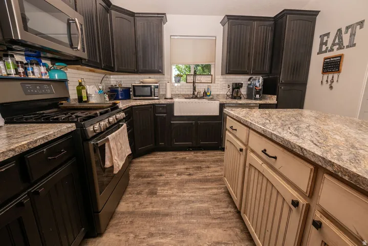 U-shaped kitchen featuring dark wood-finish cabinetry, a large kitchen island with beige cabinetry, wood-finish flooring, a stainless steel gas range, and a farmhouse sink