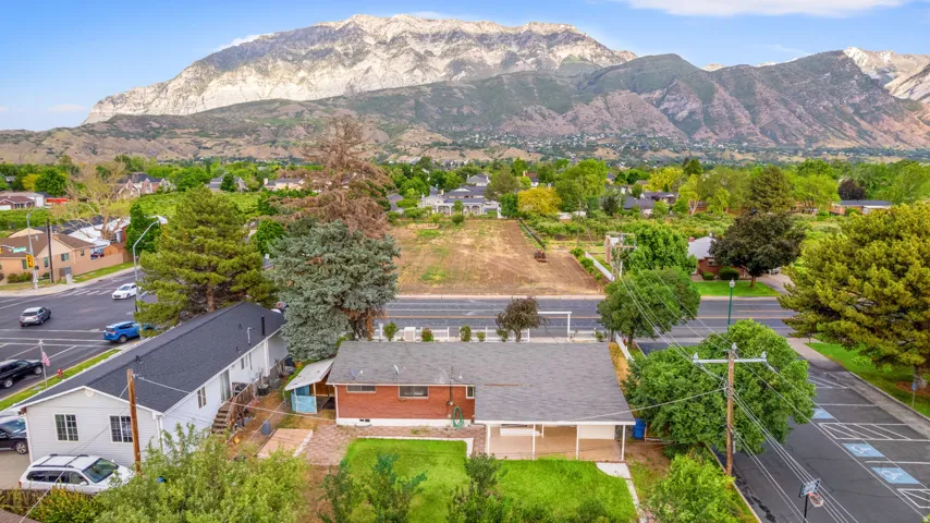 Aerial perspective showcasing a single-story residence with a dark shingle roof, brick and white siding, and an expansive mountain backdrop