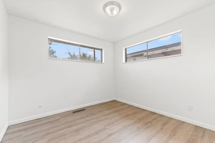 Bright room featuring two horizontal windows with aluminum frames, light wood-finish flooring, white baseboards, and a flush-mount ceiling light fixture